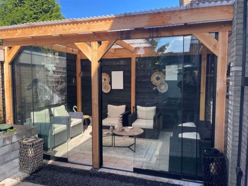 Moderne veranda met glazen wanden en comfortabele meubels, omringd door natuur.