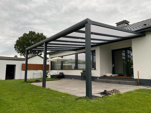 Een moderne overkapping met glazen dak naast een huis op een groene grasmat.