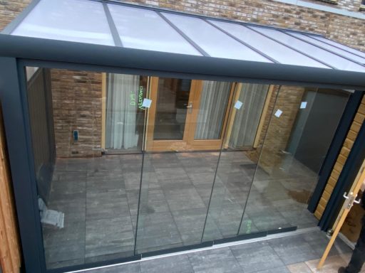 Moderne serre met glazen wanden en houten deuren, op een betegelde vloer.