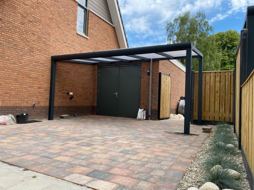 Moderne carport met glazen dak en stenen oprit naast een huis.